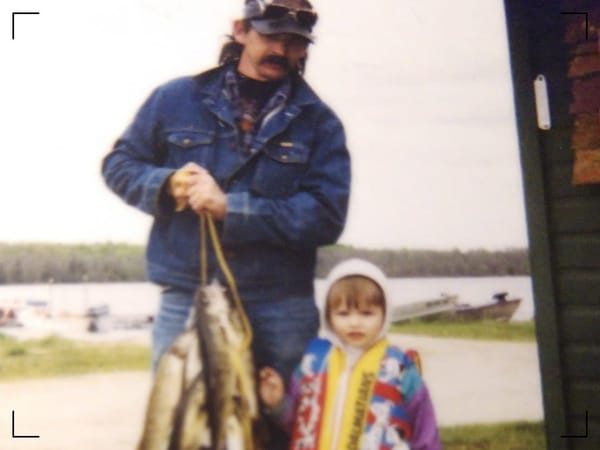 A man, 39, with long dark hair and a thick dark moustache. He holds a catch of walleye, perch, and northern pike. Next to him is a three year old in a 101 Dalmatians-themed life vest.